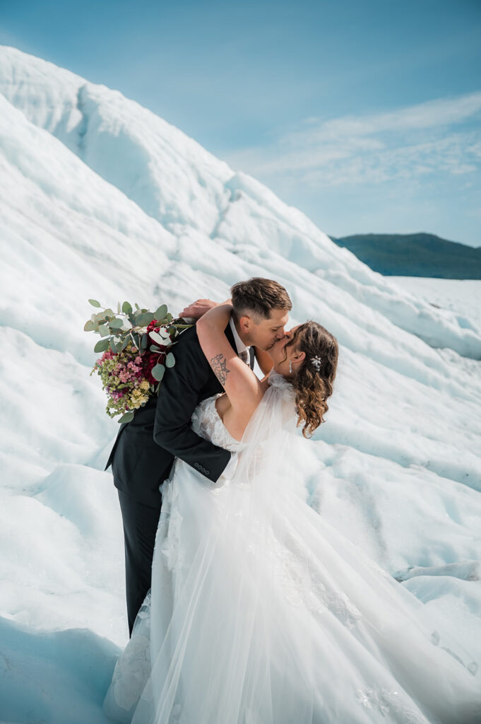 bride and groom kissing while holding a bouquet of flowers during their alaska glacier elopement 