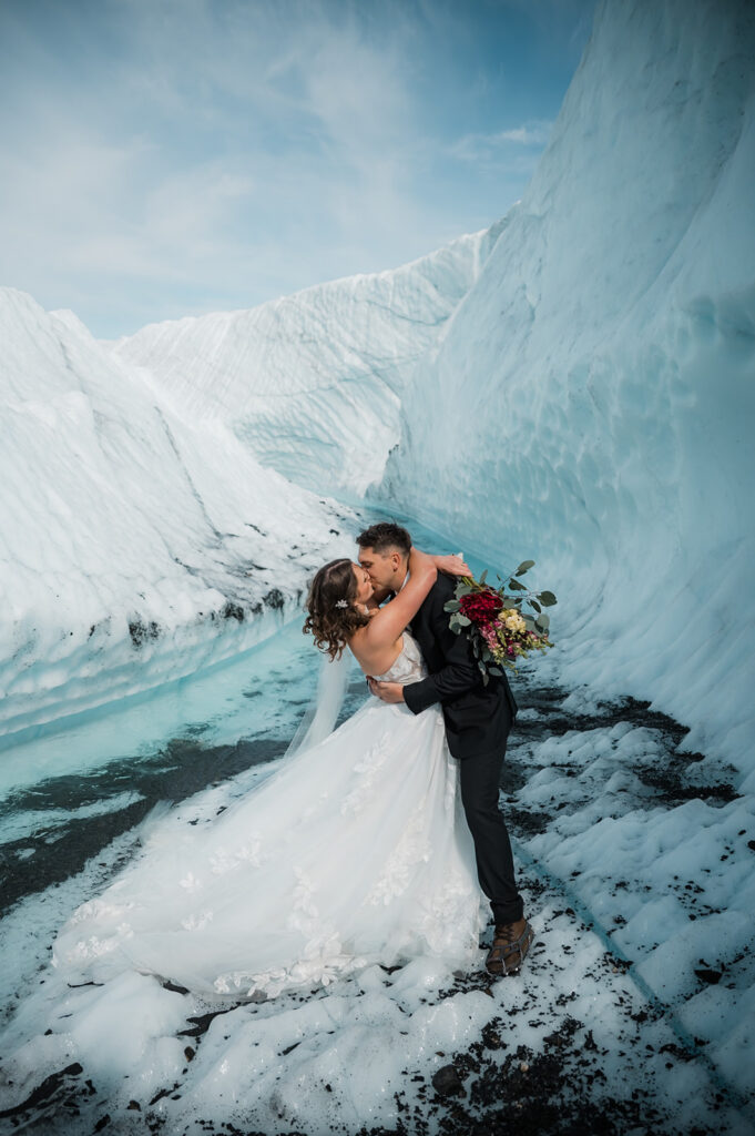 bride and groom share their first kiss surrounded by a glacial river and ice during their alaska glacier elopement on the matanuska glacier