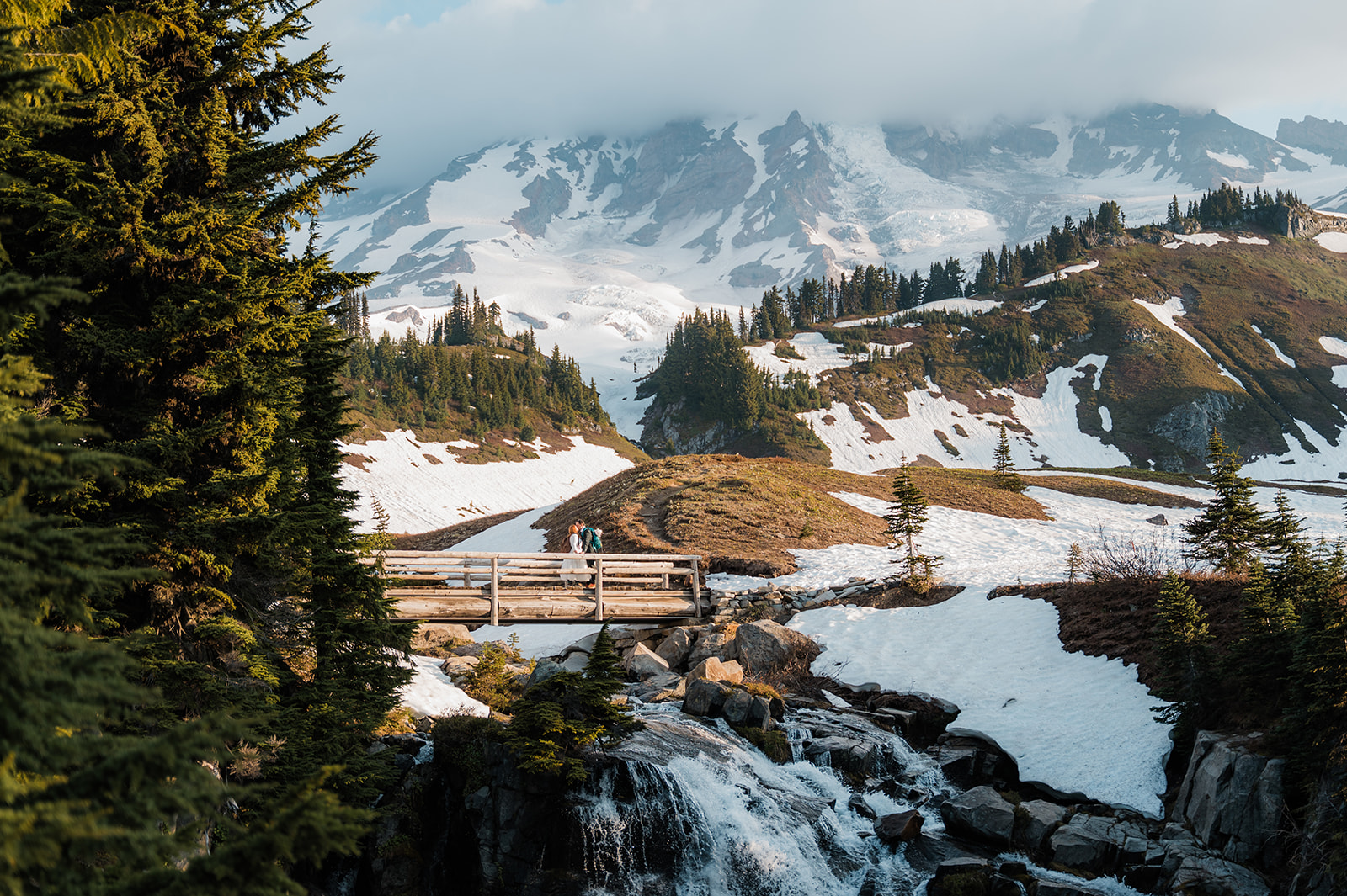 couple on their mt. rainier elopement day kissing on the bridge over Myrtle Falls with views of snowy mt. rainier in the background