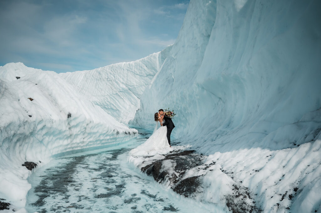 bride and groom sharing their first kiss on a glacier in alaska surrounded by turquoise water and glacial ice 
