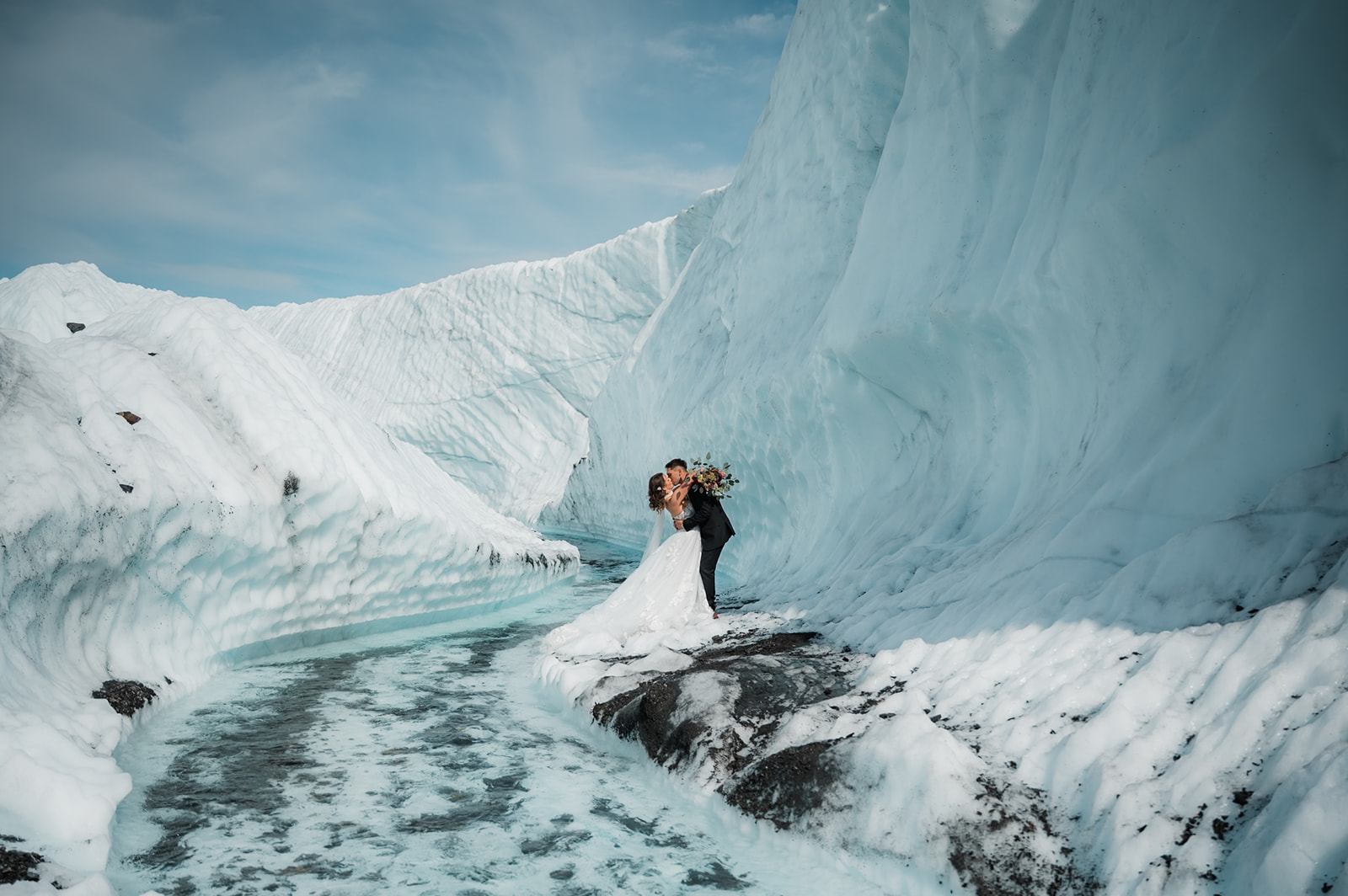 bride and groom sharing their first kiss on a glacier in alaska surrounded by turquoise water and glacial ice