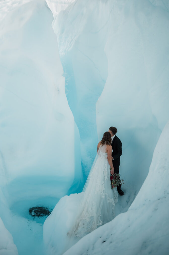 bride and groom looking at a glacial waterfall on their elopement day on the matanuska glacier