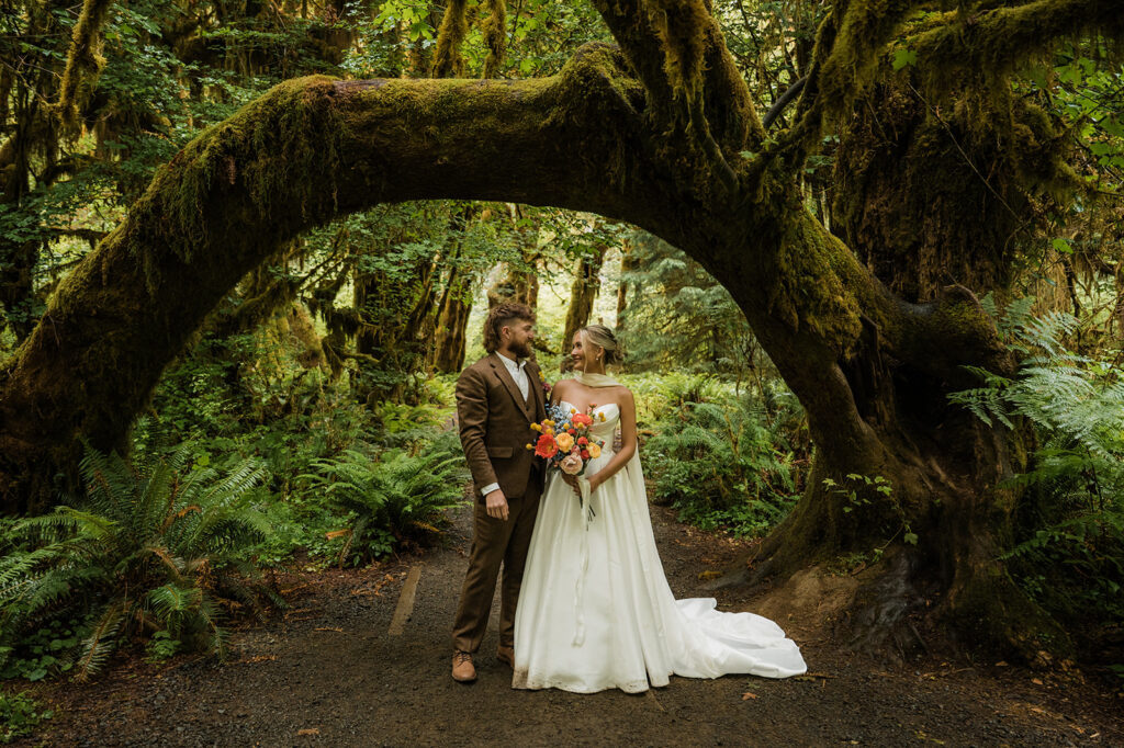 bride and groom standing under a mossy tree in the Hoh Rainforest during their PNW elopement day in Olympic National Park