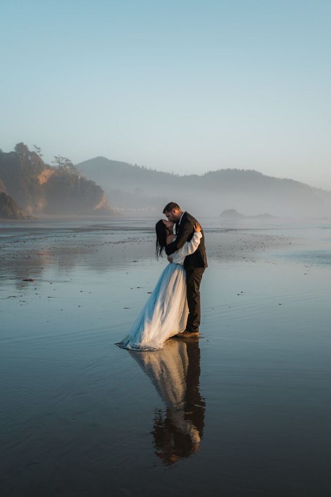 couple during their Oregon coast vow renewal kissing on the beach at hug point with their reflection in the water