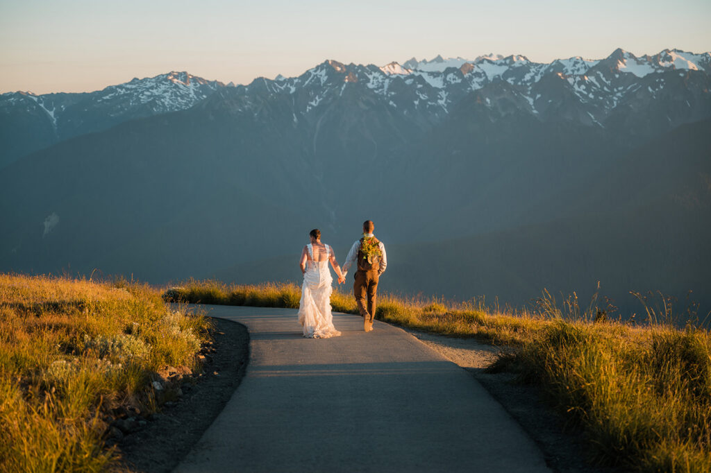 couple walking and holding with views of the mountains in the background on their hurricane ridge elopement day