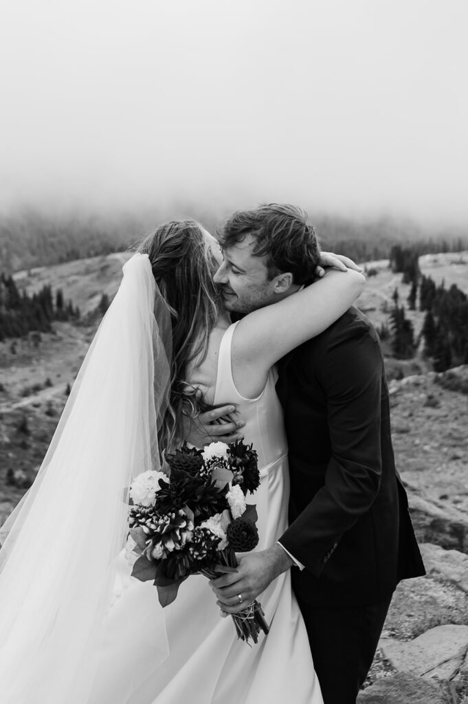 Couple embracing with soft mountain views peeking through clouds at Mt. Rainier