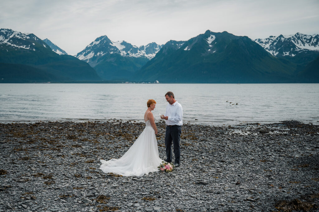 Hannah and Thad reading vows on the Seward Alaska coastline with mountain views